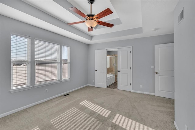 unfurnished bedroom with ceiling fan, connected bathroom, a raised ceiling, and light carpet