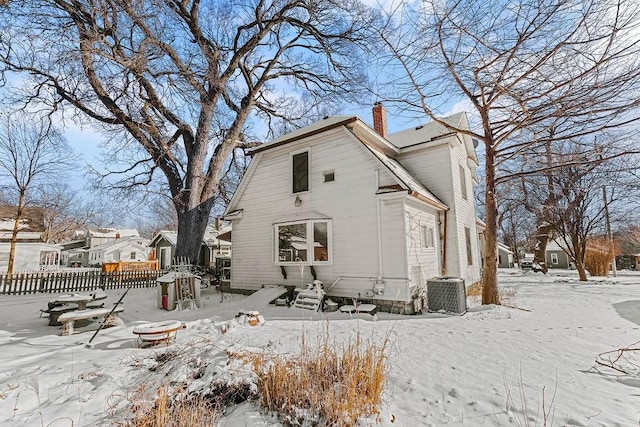 snow covered rear of property featuring central air condition unit and an outdoor fire pit