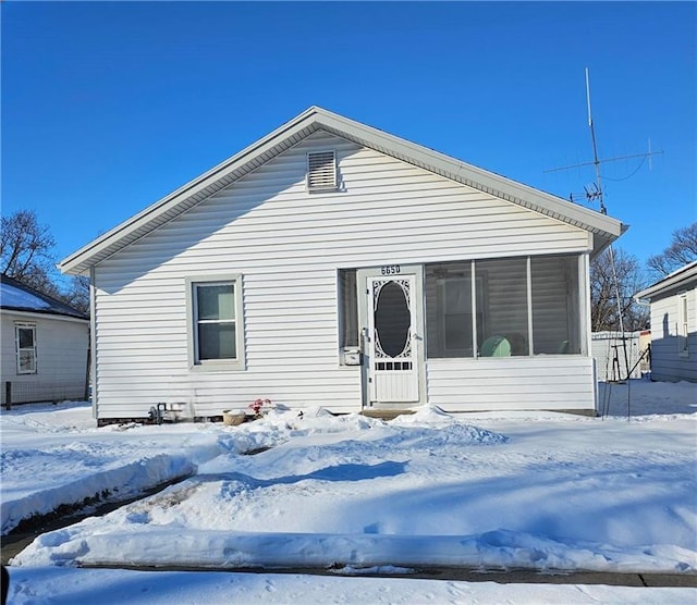 snow covered back of property featuring a sunroom