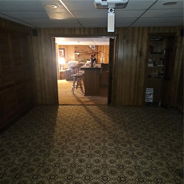 basement with a paneled ceiling, bar area, wood walls, and carpet flooring