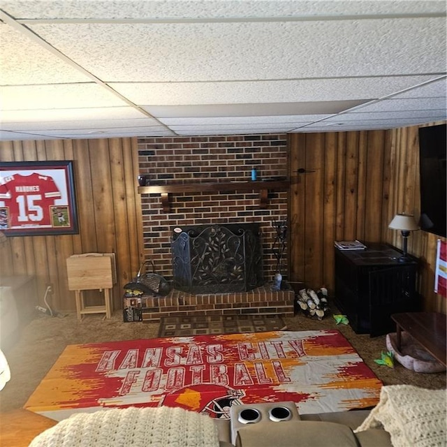 living room with a paneled ceiling, wood walls, and a fireplace