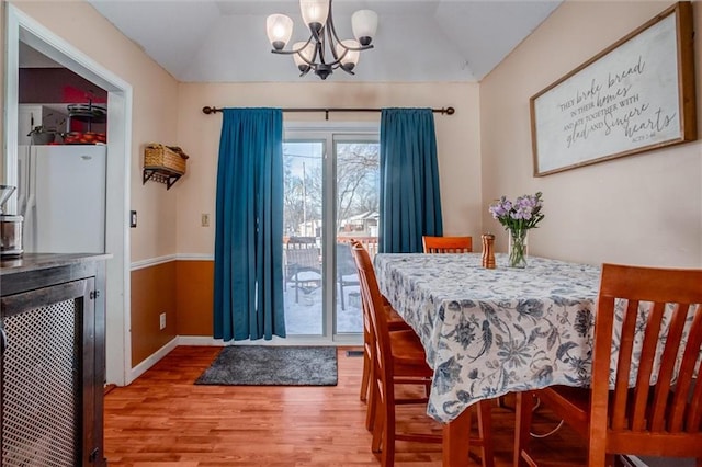 dining space with an inviting chandelier, lofted ceiling, and wood-type flooring