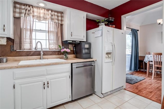 kitchen with white refrigerator with ice dispenser, stainless steel dishwasher, white cabinets, light tile patterned flooring, and sink