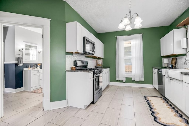 kitchen featuring decorative light fixtures, white cabinets, a textured ceiling, a chandelier, and appliances with stainless steel finishes