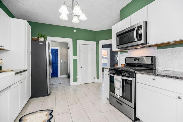 kitchen with appliances with stainless steel finishes, white cabinetry, an inviting chandelier, and a textured ceiling