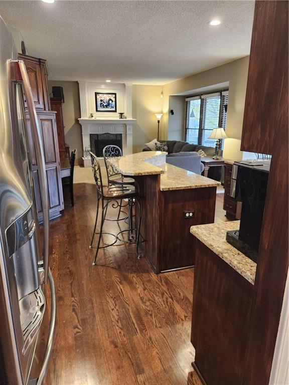 kitchen with a center island, light stone counters, a large fireplace, dark hardwood / wood-style floors, and a breakfast bar