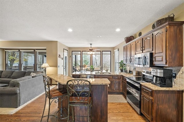 kitchen with appliances with stainless steel finishes, plenty of natural light, light stone counters, and a breakfast bar area