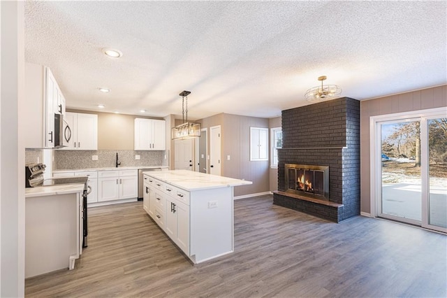 kitchen with white cabinetry, a textured ceiling, appliances with stainless steel finishes, a kitchen island, and pendant lighting