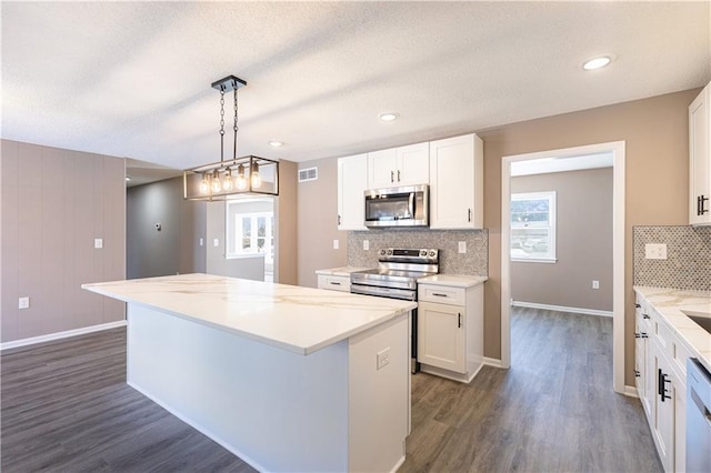 kitchen featuring dark wood-type flooring, appliances with stainless steel finishes, white cabinetry, a center island, and decorative light fixtures