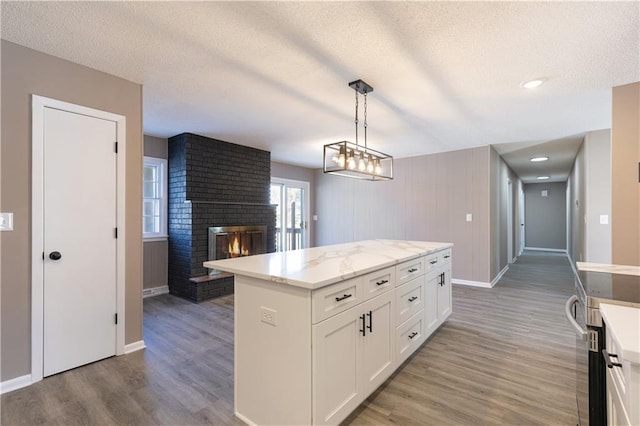 kitchen featuring hardwood / wood-style flooring, a fireplace, white cabinets, a kitchen island, and decorative light fixtures