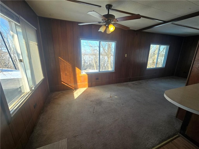 unfurnished living room with ceiling fan, carpet floors, and wood walls