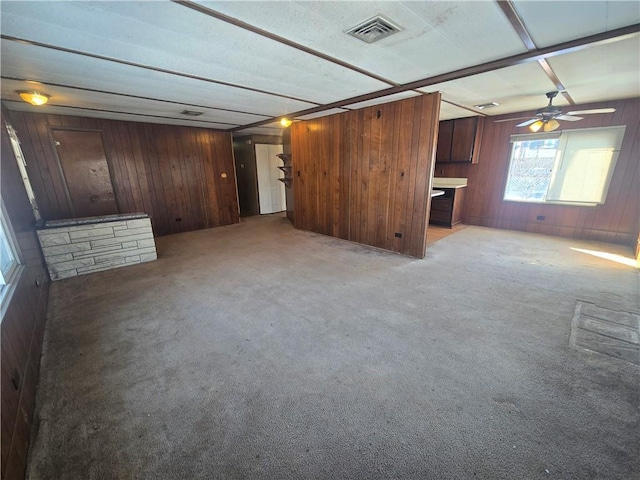 unfurnished living room with ceiling fan, light carpet, and wood walls