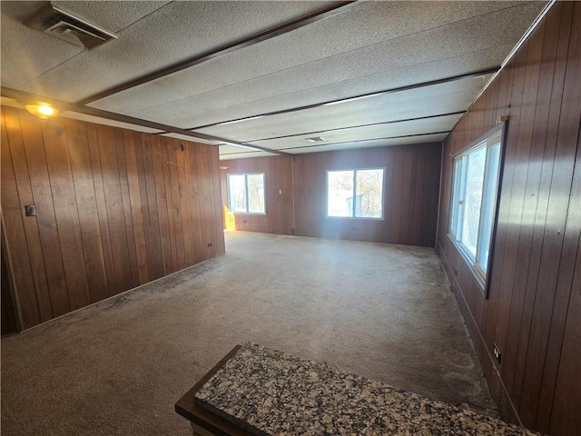 carpeted spare room featuring wood walls and a textured ceiling