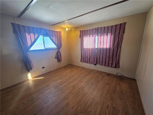 spare room featuring a textured ceiling, wood walls, and wood-type flooring