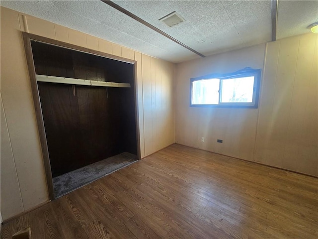 unfurnished bedroom with a textured ceiling, a closet, wood walls, and hardwood / wood-style flooring