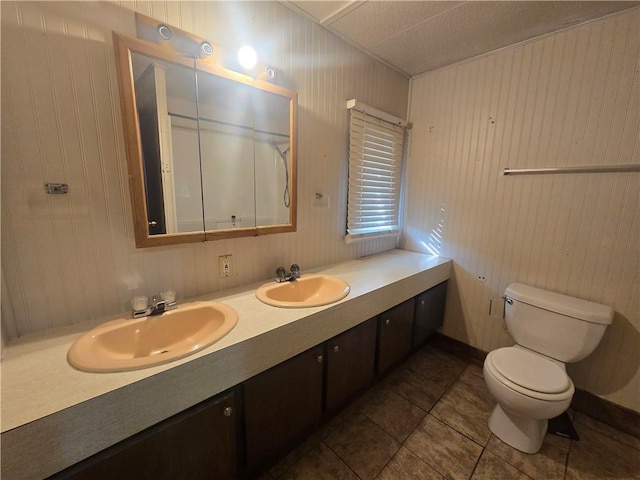 bathroom with toilet, wooden walls, vanity, and tile patterned floors