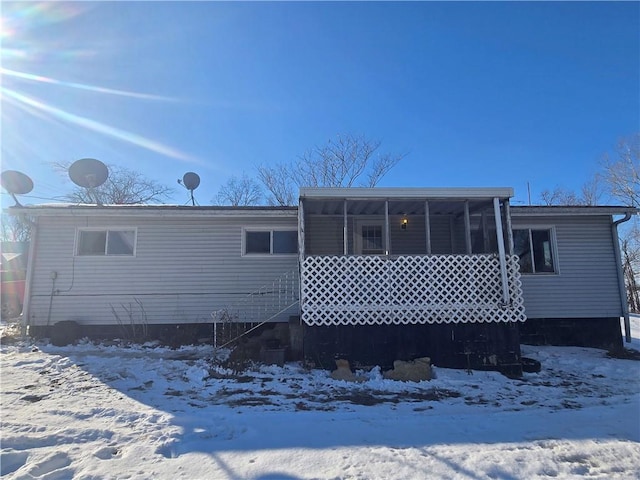 snow covered rear of property featuring a sunroom