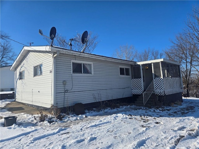 snow covered rear of property with a sunroom