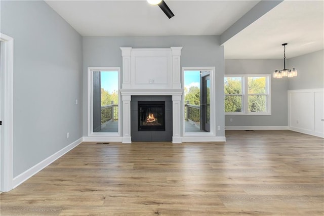 unfurnished living room with ceiling fan with notable chandelier, light wood-type flooring, and a tiled fireplace