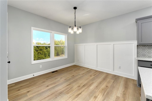 unfurnished dining area featuring light wood-type flooring and a notable chandelier