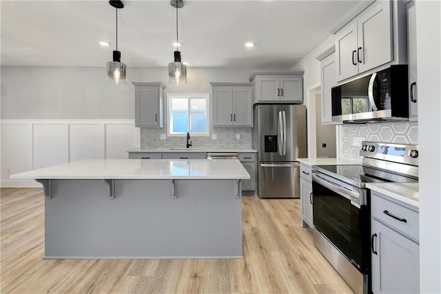 kitchen with pendant lighting, a kitchen island, a breakfast bar, gray cabinetry, and appliances with stainless steel finishes