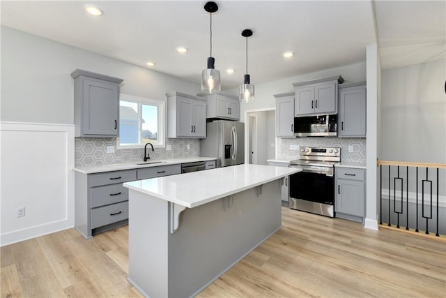 kitchen featuring gray cabinets, appliances with stainless steel finishes, a breakfast bar, sink, and decorative light fixtures