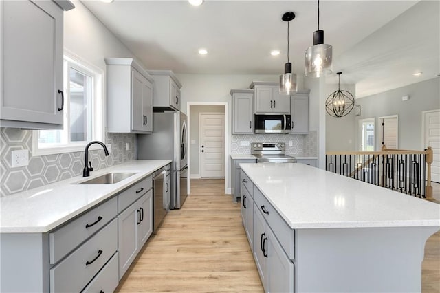 kitchen with pendant lighting, a kitchen island, gray cabinets, appliances with stainless steel finishes, and sink