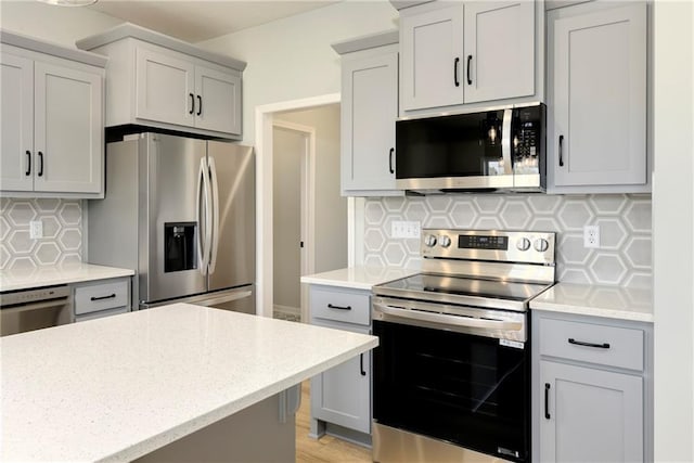 kitchen featuring light stone countertops, gray cabinets, backsplash, and appliances with stainless steel finishes