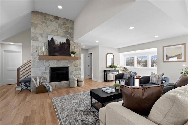 living room featuring light hardwood / wood-style flooring, a stone fireplace, and lofted ceiling