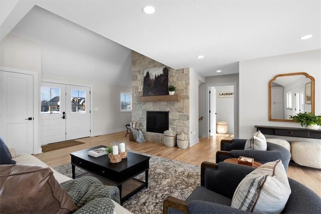 living room with lofted ceiling, light wood-type flooring, french doors, and a stone fireplace