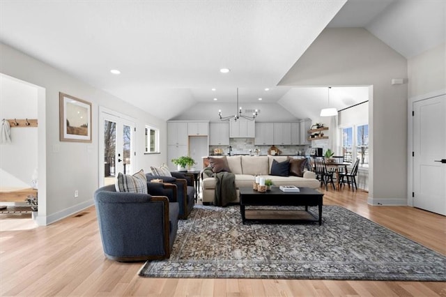 living room featuring lofted ceiling, french doors, light wood-type flooring, and a notable chandelier