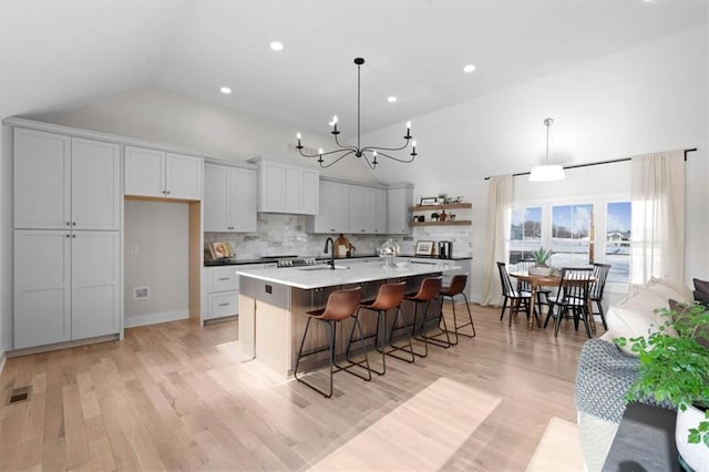 kitchen featuring a kitchen bar, a kitchen island with sink, backsplash, and hanging light fixtures