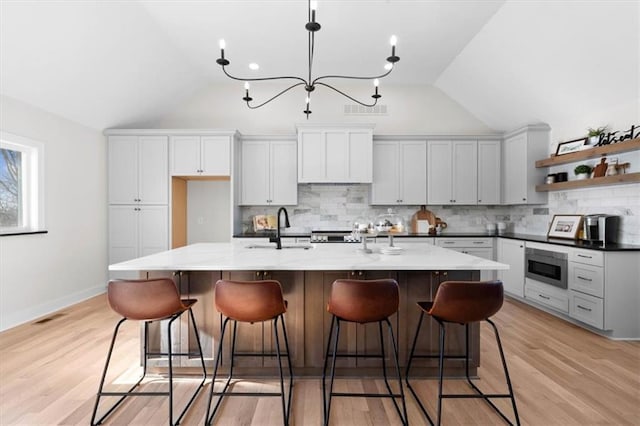 kitchen with sink, vaulted ceiling, tasteful backsplash, a center island with sink, and stainless steel microwave