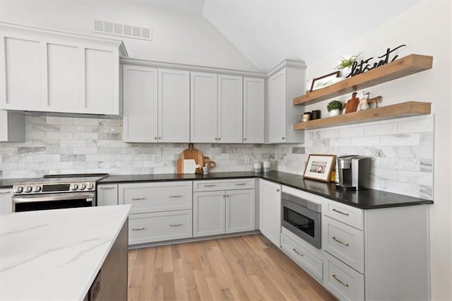 kitchen featuring vaulted ceiling, light hardwood / wood-style floors, stainless steel appliances, dark stone counters, and tasteful backsplash