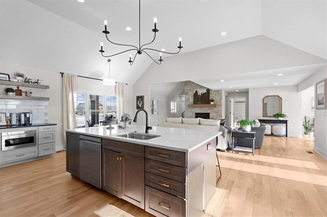 kitchen with stainless steel appliances, sink, vaulted ceiling, light wood-type flooring, and a stone fireplace