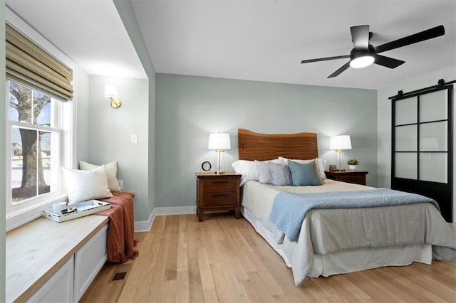 bedroom with light wood-type flooring, ceiling fan, and a barn door