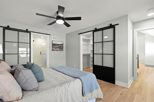 bedroom featuring a spacious closet, connected bathroom, ceiling fan, a closet, and a barn door