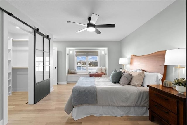 bedroom featuring ceiling fan, light hardwood / wood-style floors, and a barn door