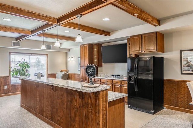 kitchen with a kitchen bar, wood walls, black fridge, decorative light fixtures, and beamed ceiling