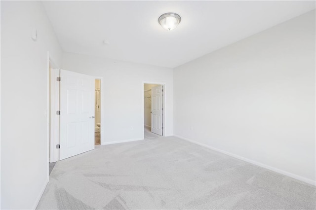 unfurnished bedroom featuring connected bathroom, a spacious closet, light colored carpet, and a closet