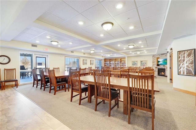 carpeted dining room with a stone fireplace and beam ceiling