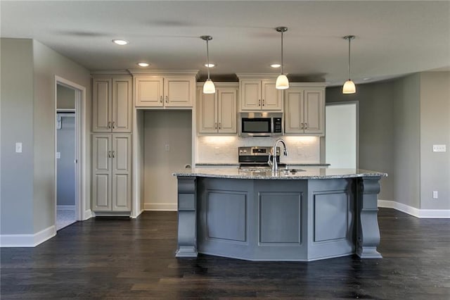 kitchen featuring light stone counters, pendant lighting, stainless steel appliances, a kitchen island with sink, and sink