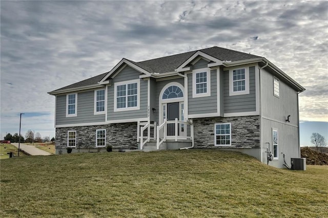 raised ranch featuring central air condition unit, a front yard, and stone siding