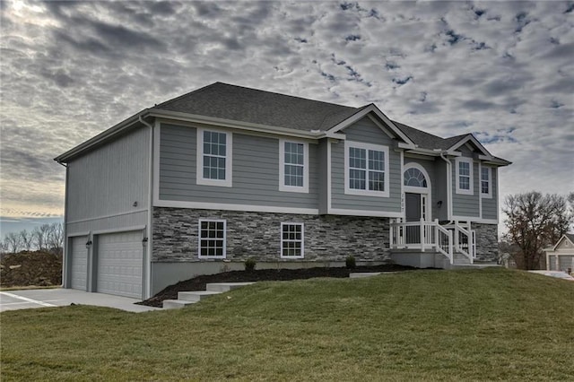 raised ranch with stone siding, a garage, concrete driveway, and a front yard