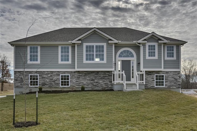 bi-level home featuring a front lawn, stone siding, and a shingled roof