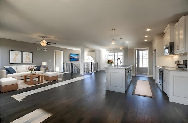 kitchen featuring a sink, stainless steel microwave, open floor plan, gas range oven, and white cabinets