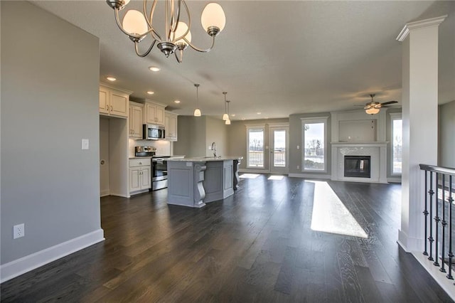 kitchen featuring a kitchen island with sink, dark wood-style flooring, a sink, stainless steel appliances, and ceiling fan with notable chandelier