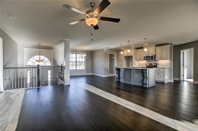 unfurnished living room with dark wood-type flooring, ceiling fan with notable chandelier, baseboards, and a sink