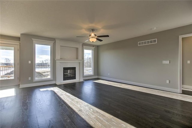 unfurnished living room featuring visible vents, baseboards, dark wood finished floors, a fireplace, and ceiling fan