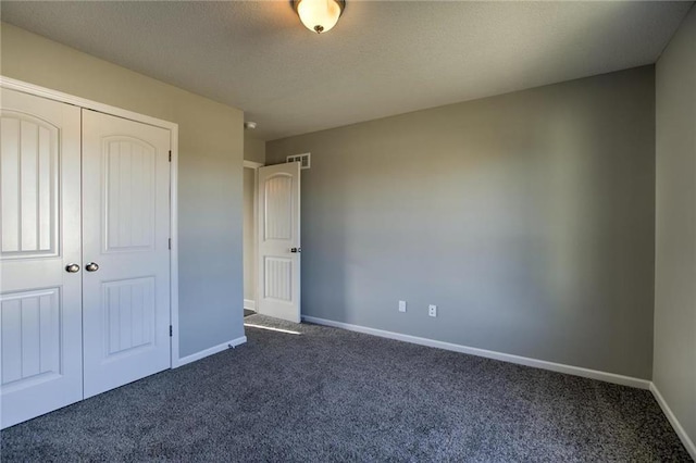 unfurnished bedroom featuring visible vents, a textured ceiling, dark carpet, a closet, and baseboards